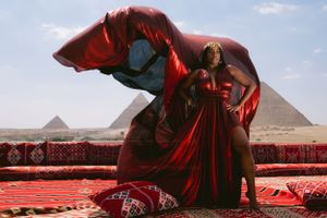 Red fabric flowing dramatically against pyramid backdrop on traditional carpet setting.