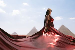 Dramatic red dress flows elegantly against Egyptian pyramid landscape.