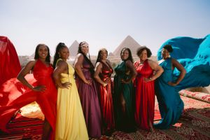 Groups pose in colorful flowing dresses against pyramids backdrop with fabric flowing in the wind.