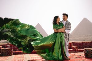 Flowing green dress catches wind as couple poses in front of Egyptian pyramids.