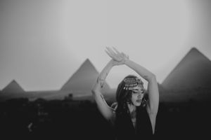 Black and white silhouette of raised arms with pyramids in the misty background.