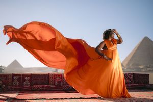Orange flowing fabric creates dynamic movement against Egyptian pyramids in dramatic desert landscape at sunset.