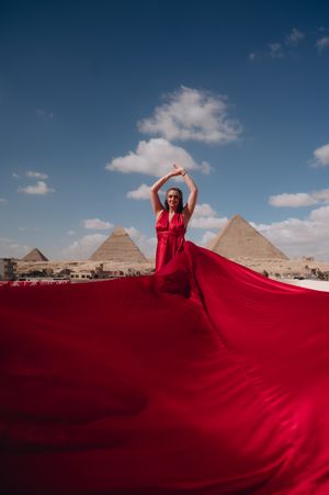 A dramatic red dress flows in the wind against the iconic pyramids of Giza backdrop.