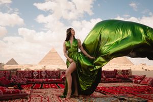 Flowing green silk dress catches wind on rooftop with pyramids in background.