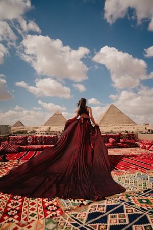 Burgundy ballgown creates dramatic silhouette against Egyptian pyramids and traditional carpets.