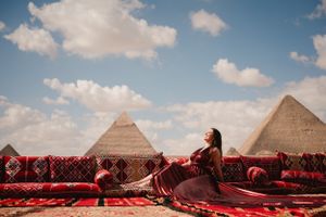 Red dress flows dramatically while posing on carpet-covered rooftop with pyramids in background.