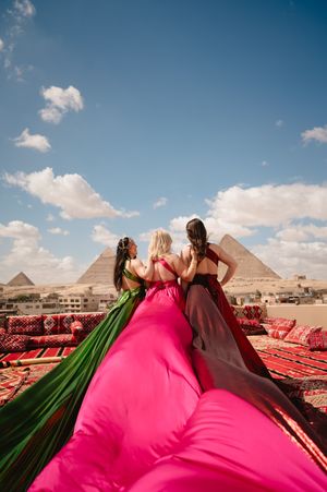Three flowing dresses in green, pink and burgundy frame pyramid view from rooftop setting.