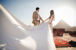 Newlyweds holding hands with flowing white dress against pyramid backdrop.