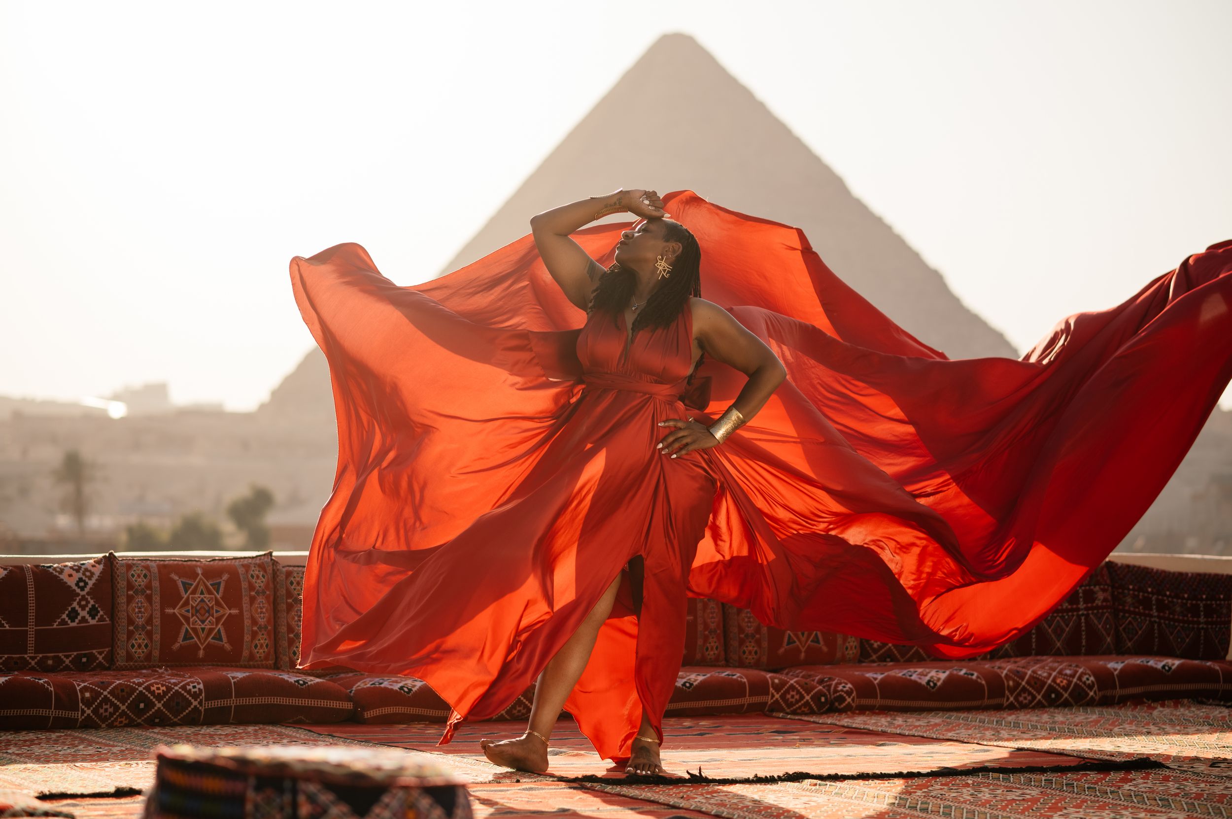 Flowing red fabric billows dramatically against an urban landscape at sunset, creating an artistic performance piece.