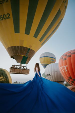 Dramatic blue dress flowing in wind with hot air balloons floating in background.