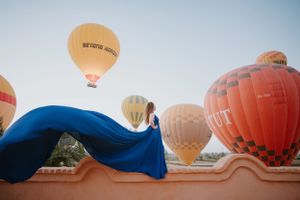 Colorful hot air balloons float against blue sky with flowing blue fabric in foreground.