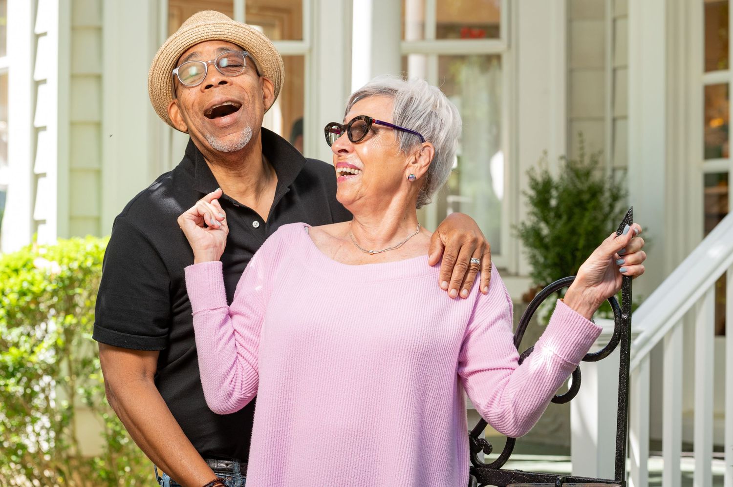 A joyful senior couple enjoying a lighthearted moment together on their front porch on a sunny day.