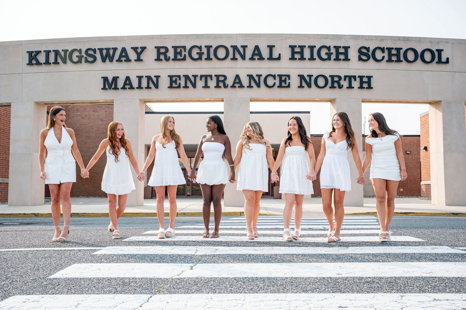 A line of people wearing white dresses and formal attire walk down steps outside a school building.
