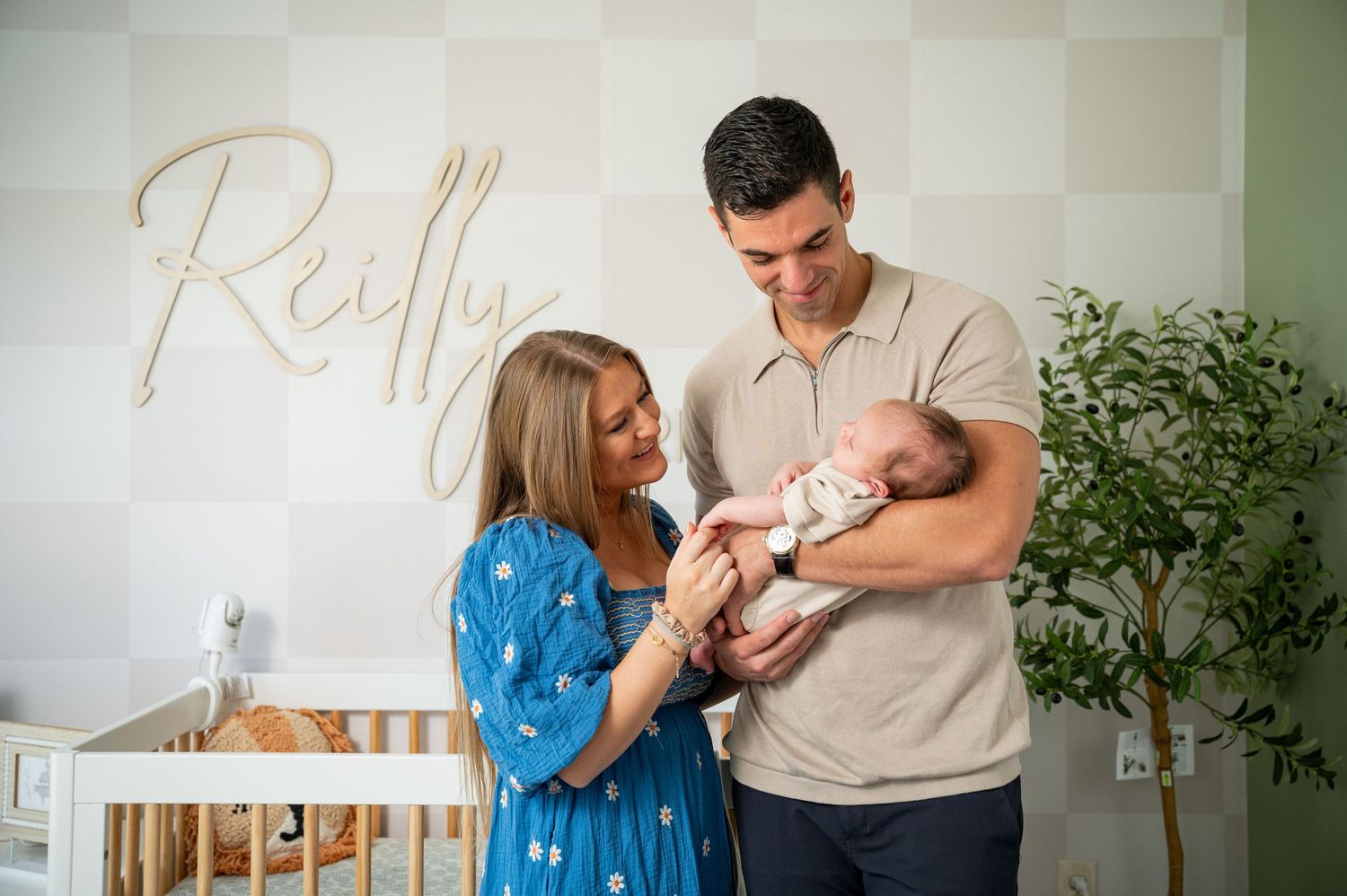 Happy parents sharing tender moment with newborn baby in nursery with custom name wall decor and greenery.