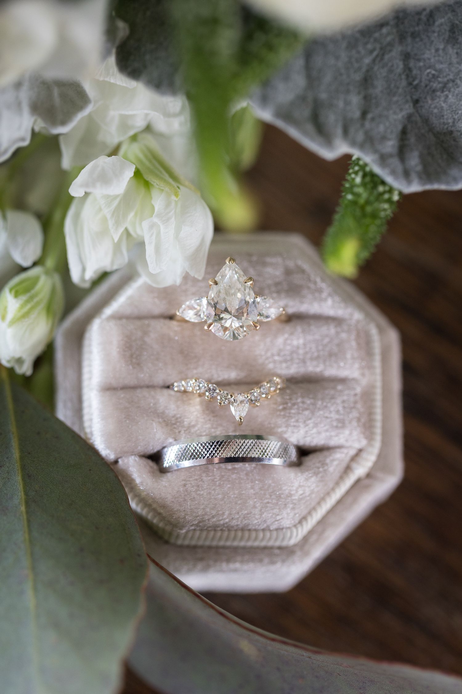 Three wedding rings displayed in a blush velvet octagonal ring box surrounded by white flowers.