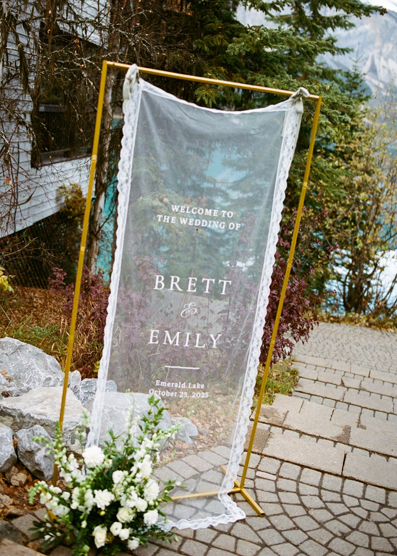 Translucent fabric banners with names printed in white text hang from golden poles along a stone paved pathway.