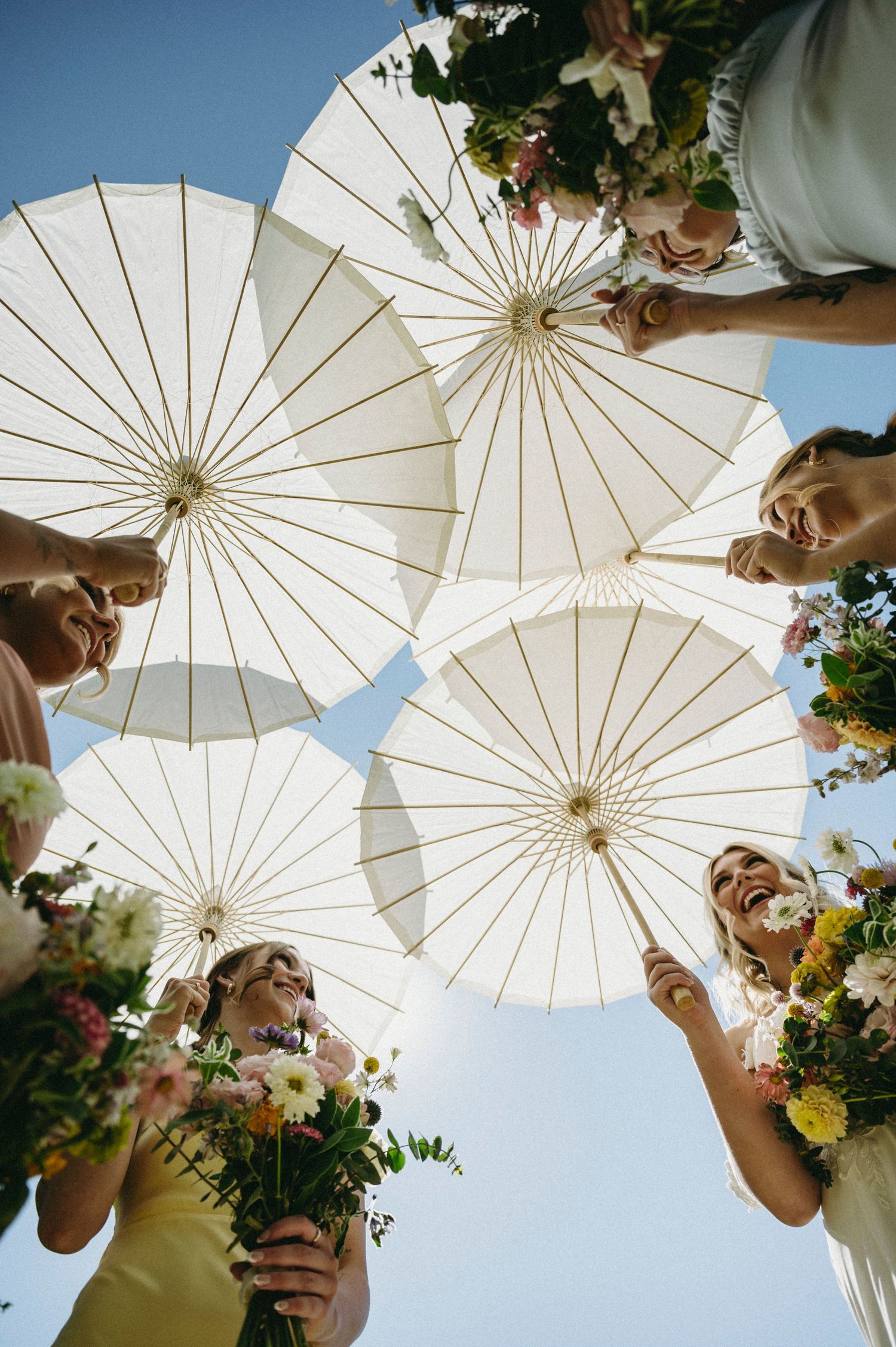Bridal party all holding parasol umbrellas looking at each other.