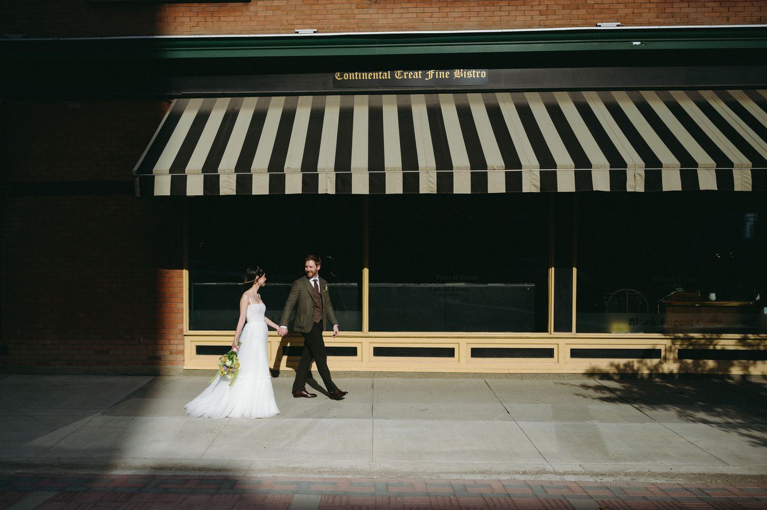A couple walks beneath a black and white striped awning on a modern storefront.