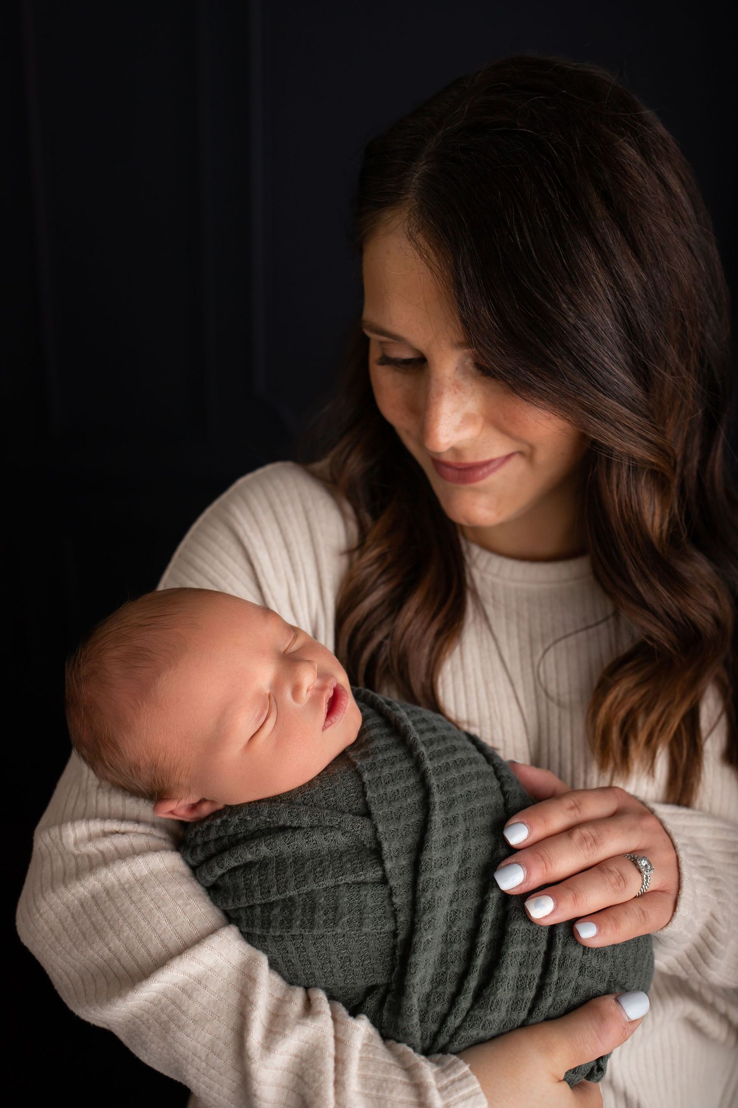 Tender moment with parent cradling sleeping swaddled newborn against dark backdrop.
