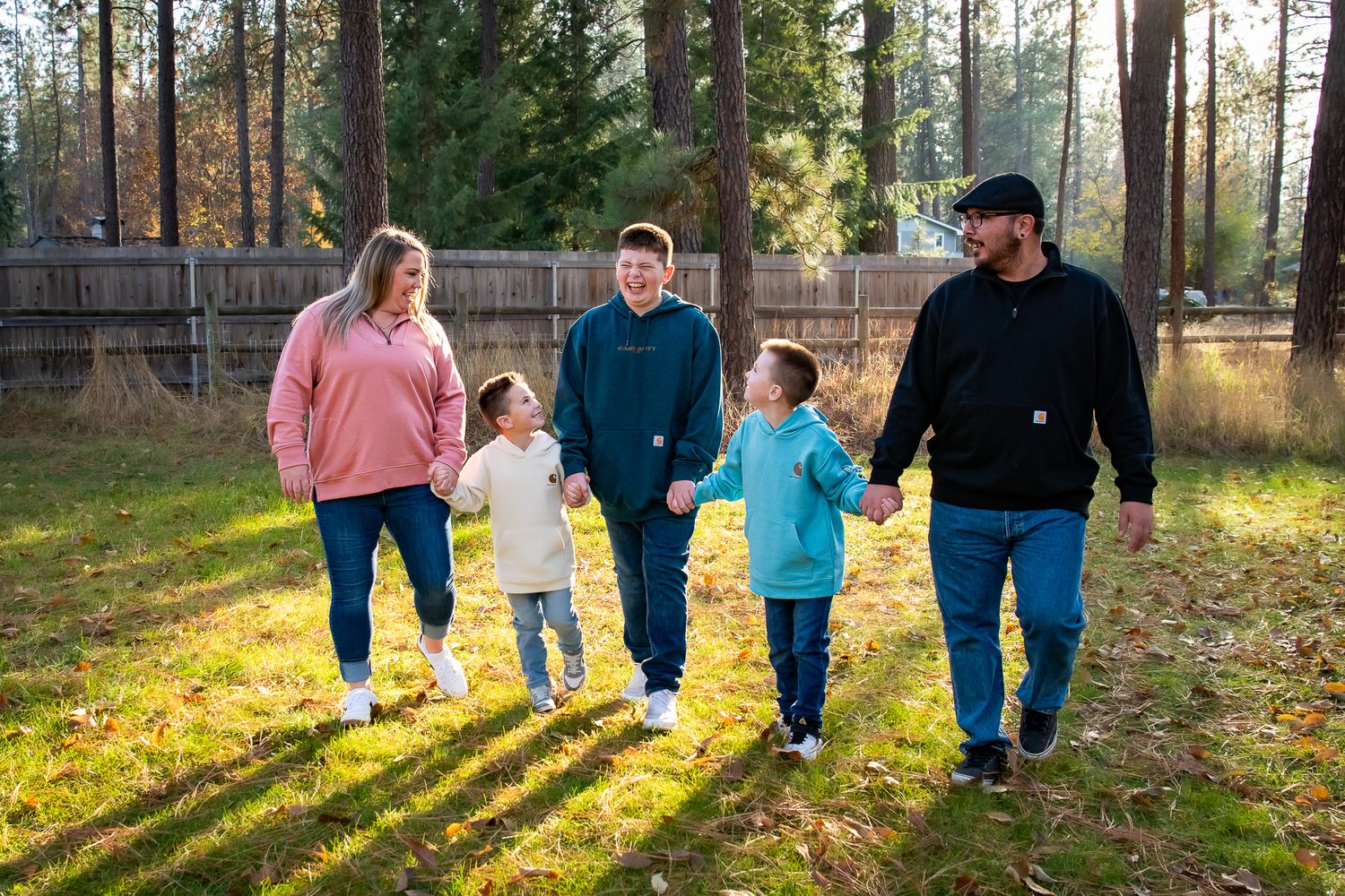 Family of four walking together on a rural road surrounded by evergreen trees.