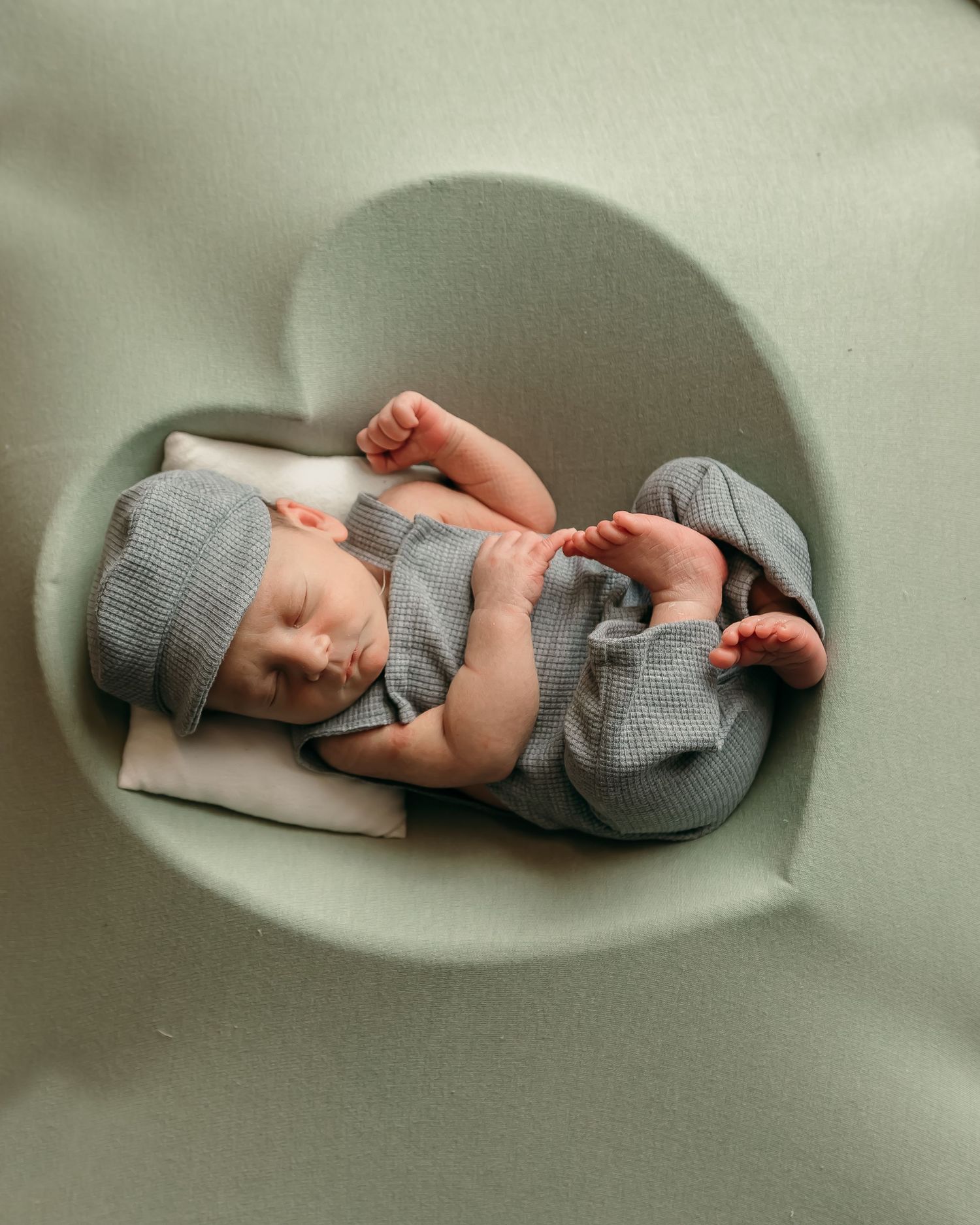 Sleeping infant in gray outfit lying in heart-shaped chair casting shadow.