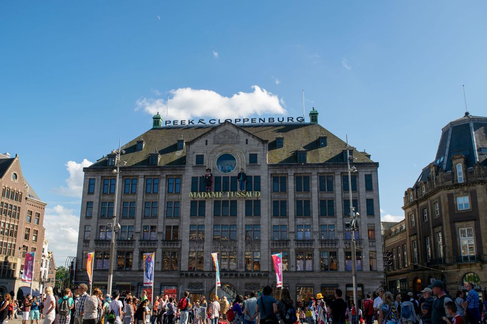 Historical Madame Tussauds building facade in Amsterdam with crowds of tourists gathering in the sunny square.