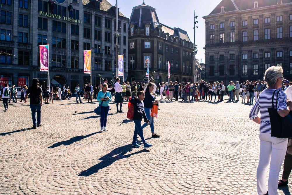 Bustling Dam Square in Amsterdam with tourists walking across the historic cobblestone plaza.
