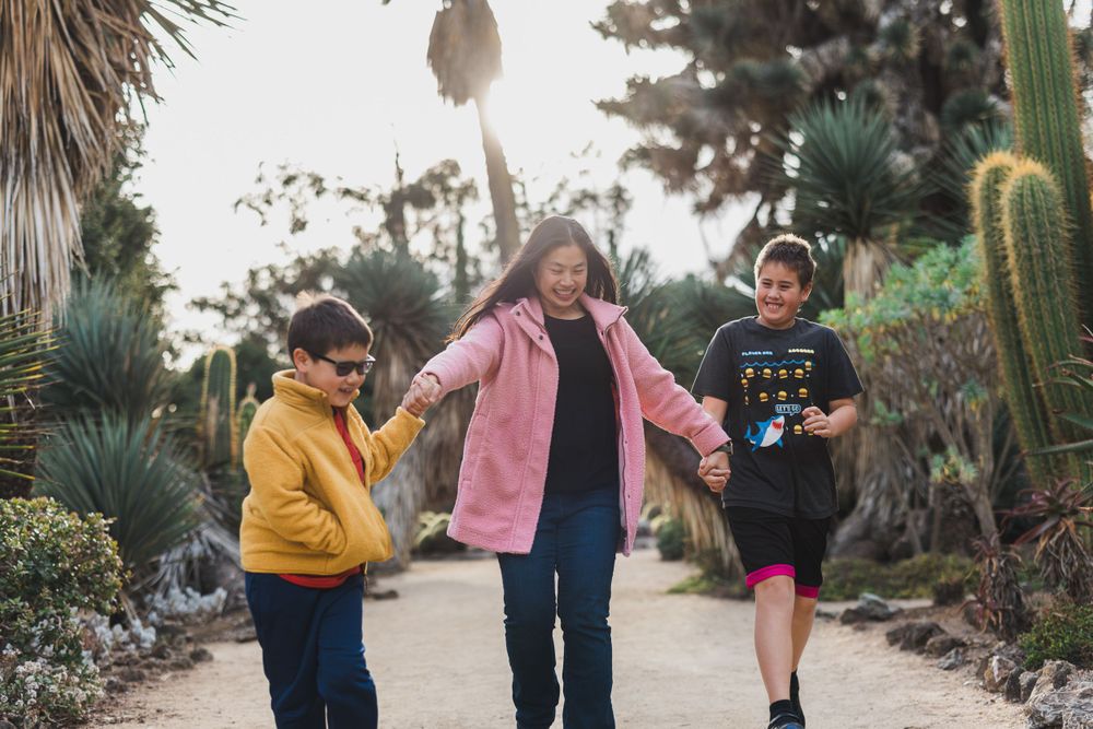 Three people holding hands while walking on a path surrounded by desert flora.