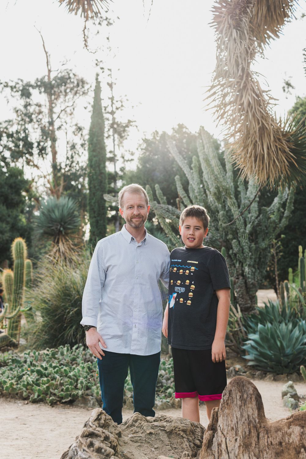 Two people standing together in a desert botanical garden surrounded by cacti and succulents.