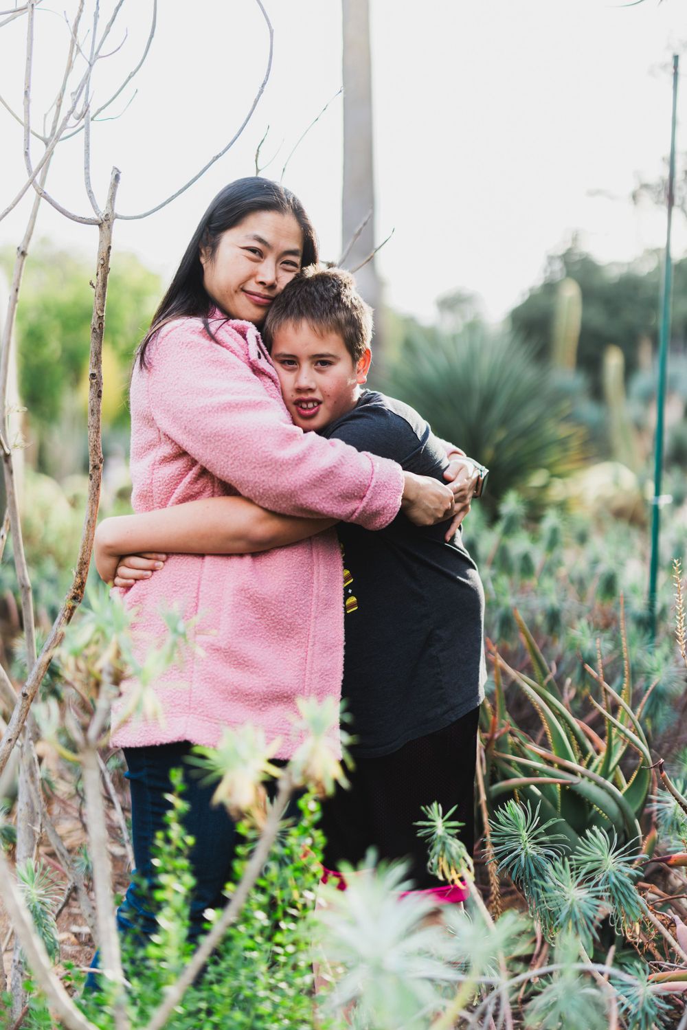 A tender embrace between two people in a garden filled with succulents and desert plants.