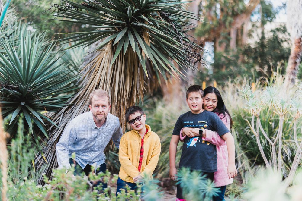 Family poses together outdoors among tropical plants and palm trees.