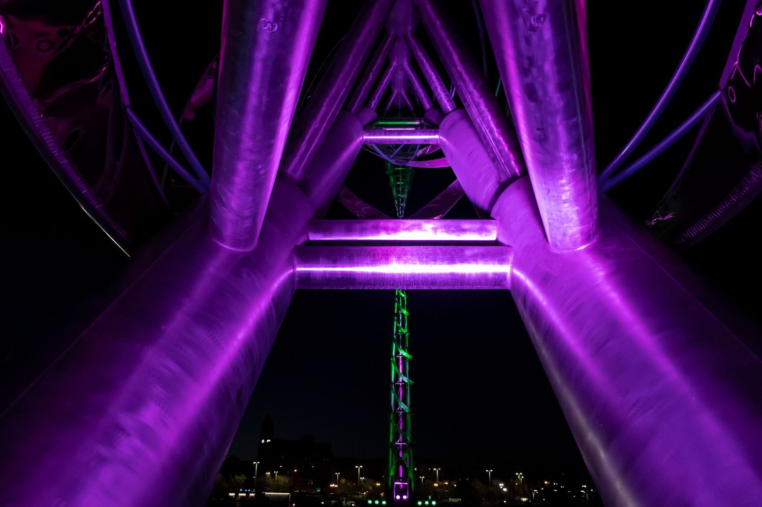 Purple-lit geometric structure frames tall building against dark night sky.