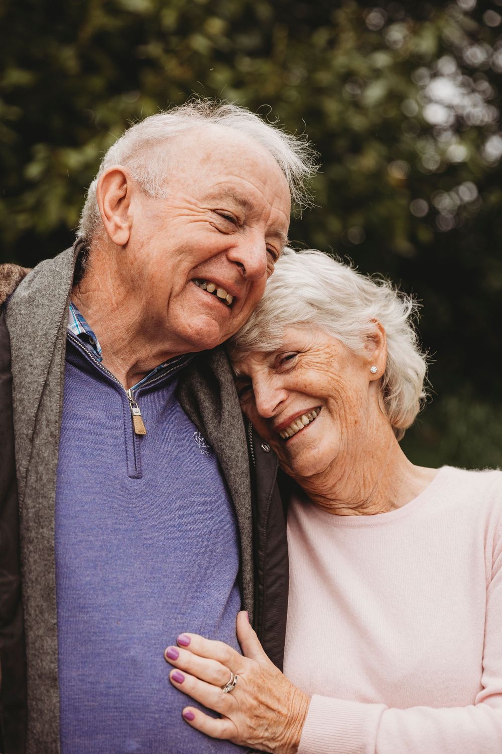 An elderly couple sharing a tender moment while smiling and laughing together outdoors.