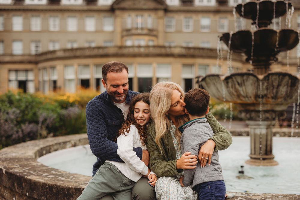 Happy family sharing a tender moment together by an ornate stone fountain in a garden setting.