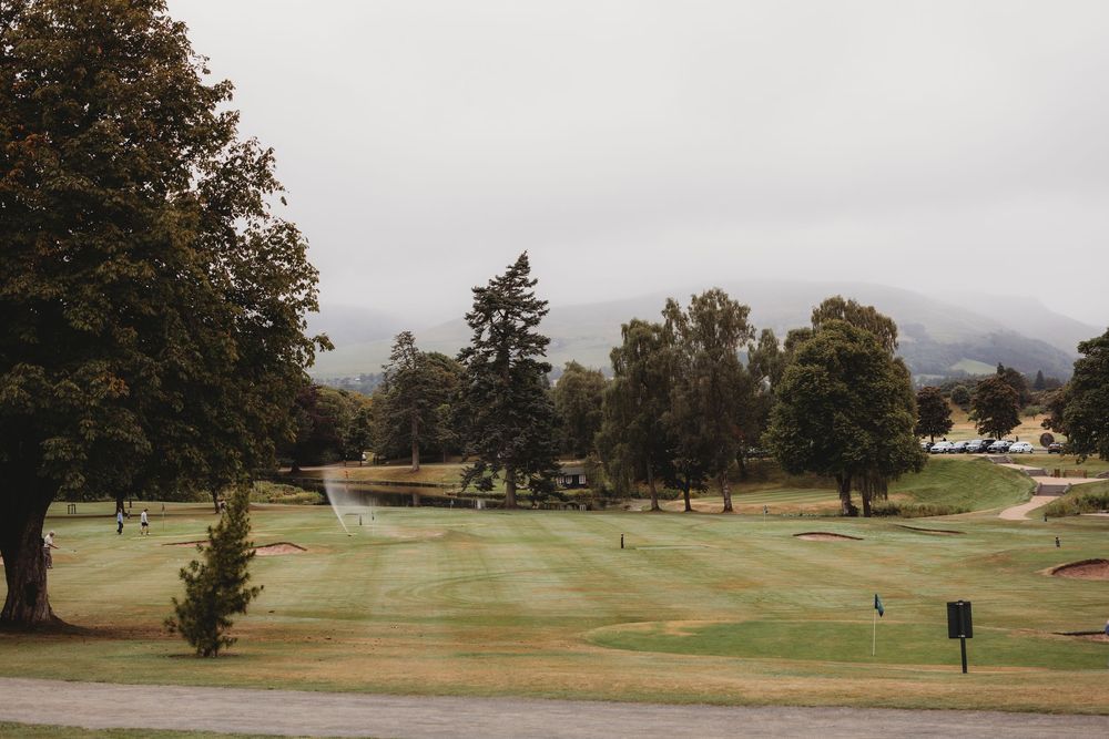 A scenic panoramic view of a misty golf course with autumn trees and rolling greens in the background.