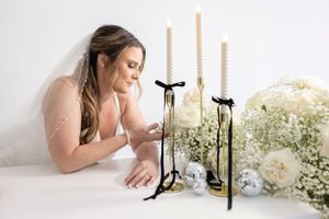 Elegant candle arrangements with gold taper holders and white floral decorations on a white table.