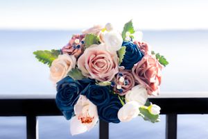 Wedding bouquet with pink and navy blue roses against an ocean backdrop.