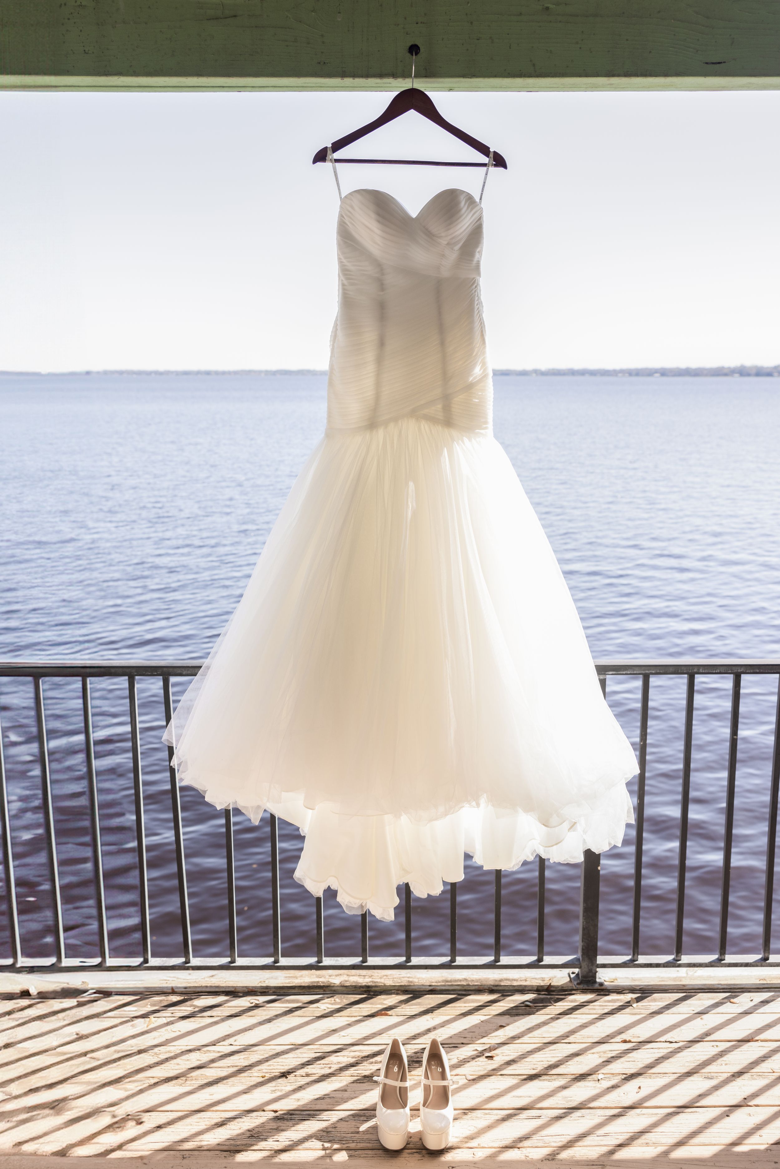 White mermaid wedding dress and shoes displayed on a waterfront balcony railing.
