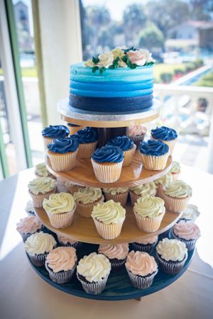 A blue gradient wedding cake with matching cupcakes arranged on a multi-tiered stand.