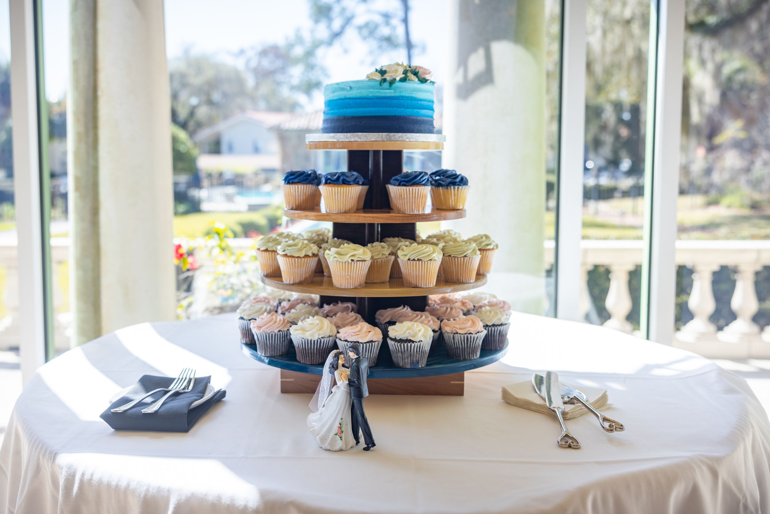 An elegant blue ombre wedding cake with cupcakes arranged on a tiered display stand.