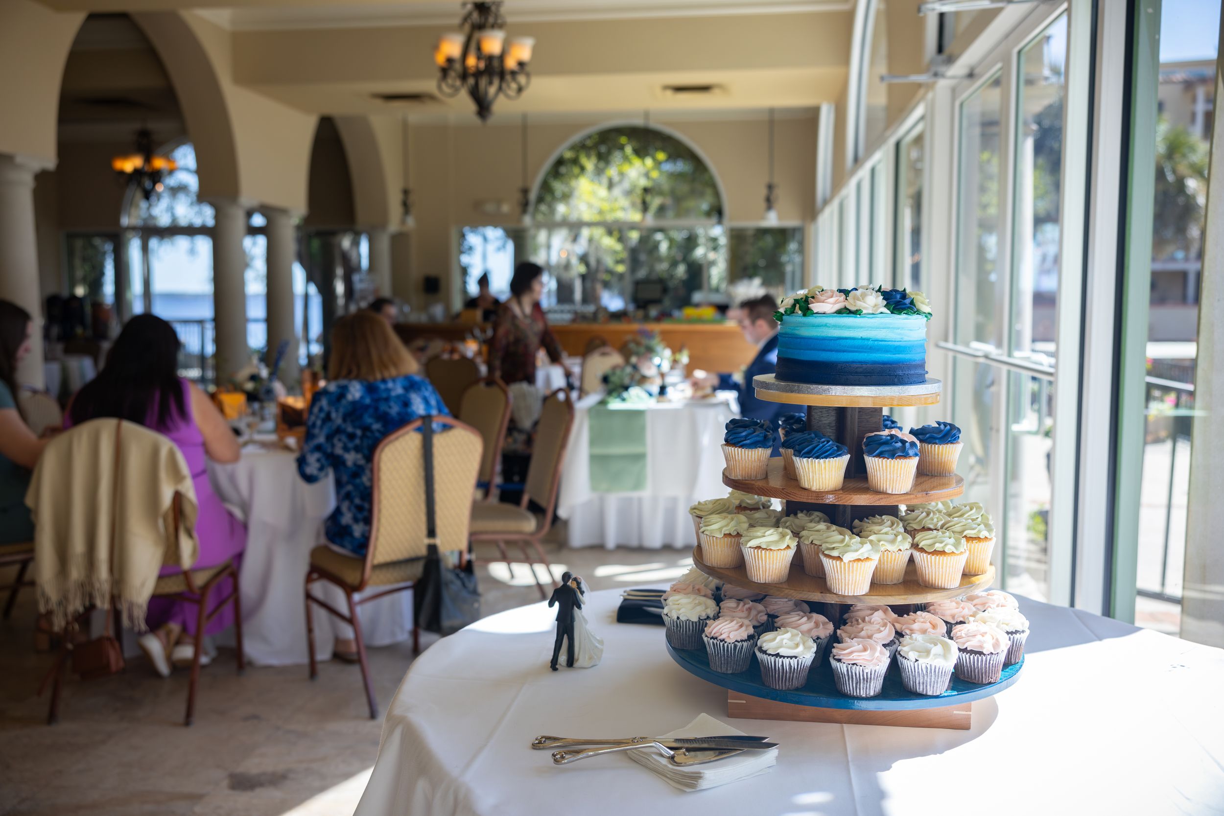A wedding reception venue with blue-themed dessert display near bright windows.