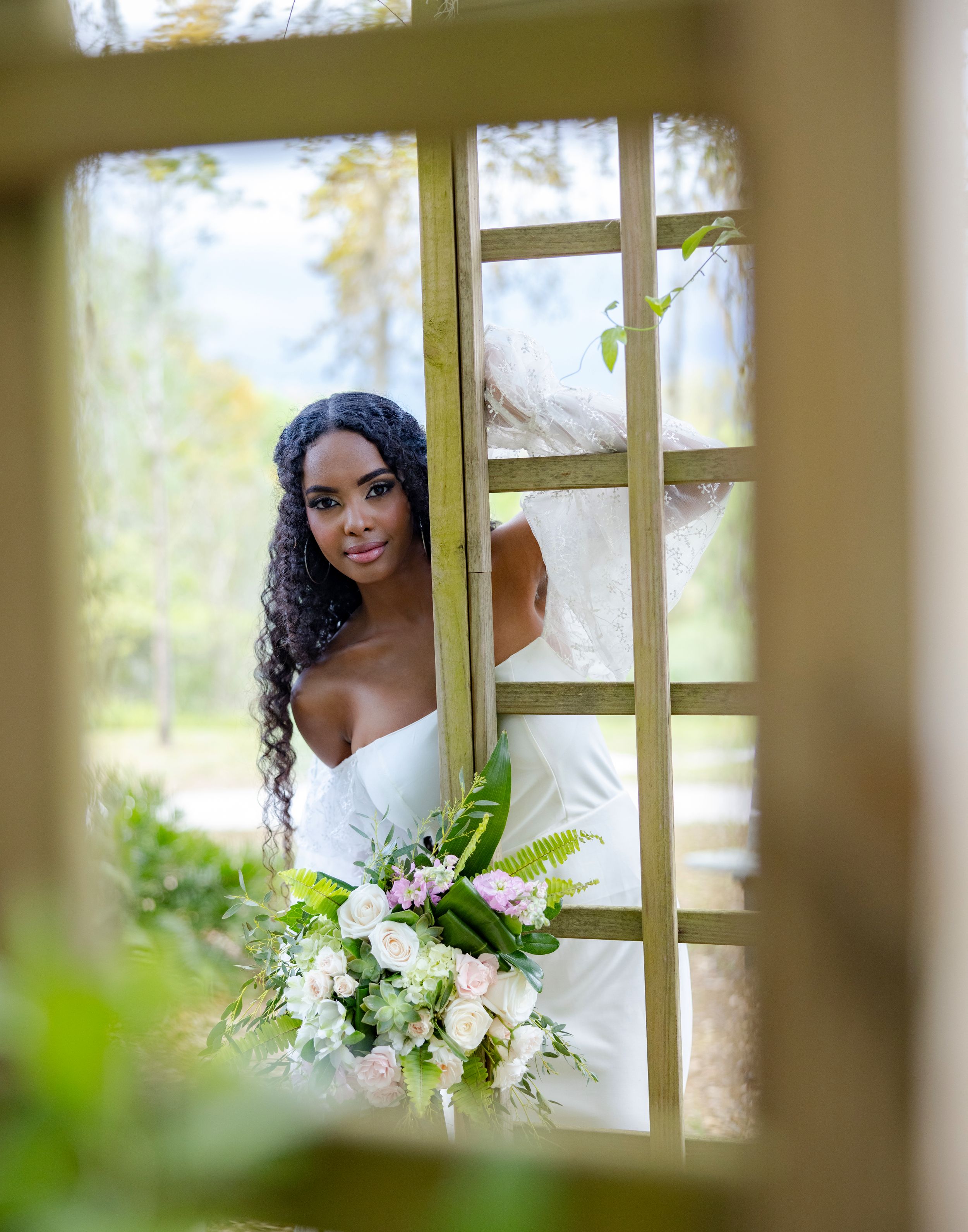 Artistic window frame composition of bride holding lush white and green bouquet.