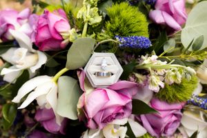 Wedding ring nestled among pink roses and green florals in elegant bouquet.