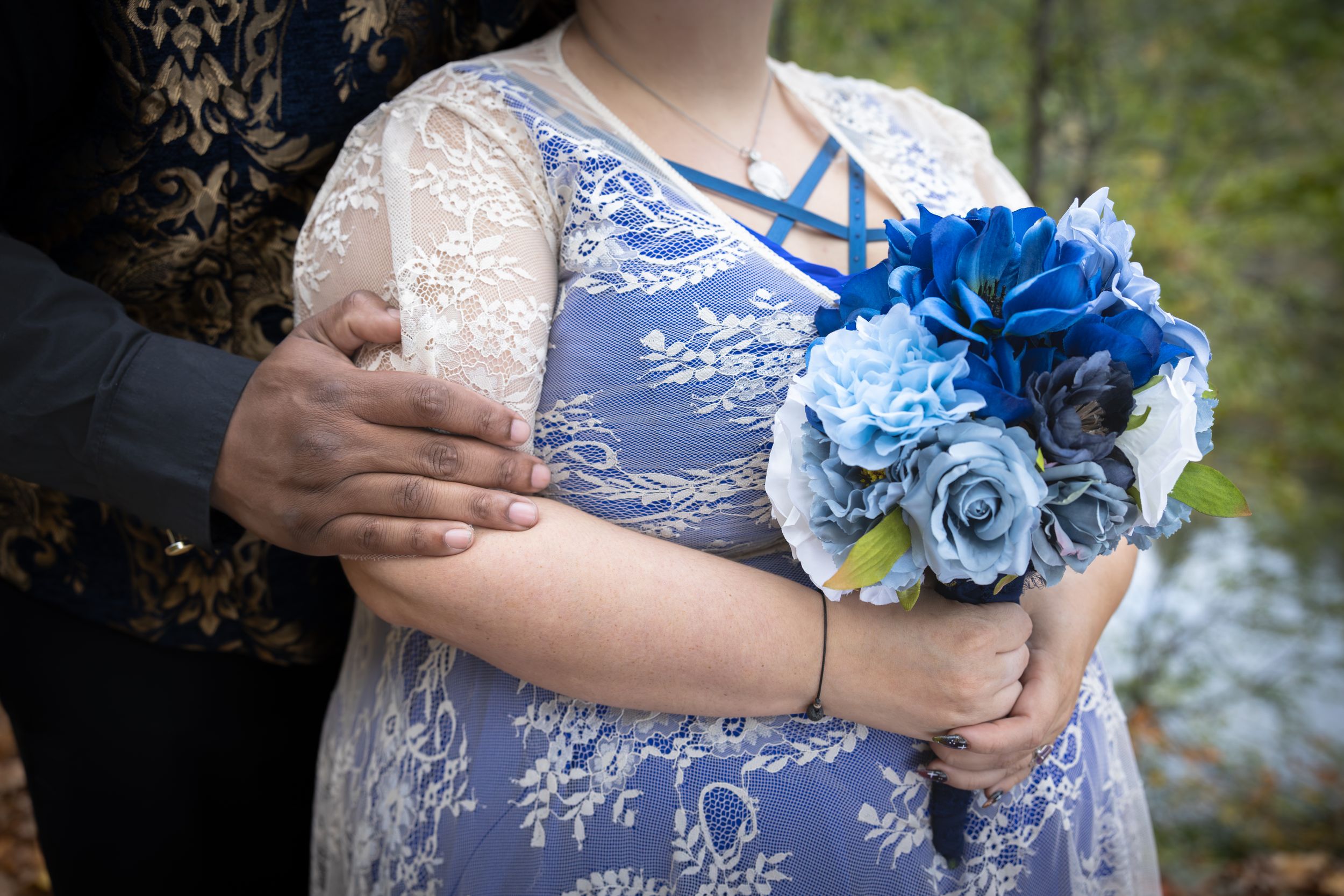 A close-up of blue floral corsage against white lace wedding attire.