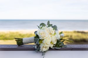 Classic white bridal bouquet with roses and eucalyptus against an ocean backdrop.