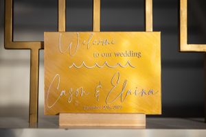 Gold wedding welcome sign with elegant cursive lettering displayed on a black background.