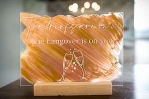 Acrylic wedding sign with champagne glass illustration and humorous hangover message.