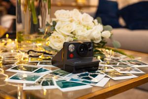 Vintage Polaroid camera with scattered wedding photos and white roses on a table.