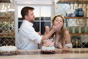 A playful moment between two people sharing cake at a rustic counter surrounded by glassware.