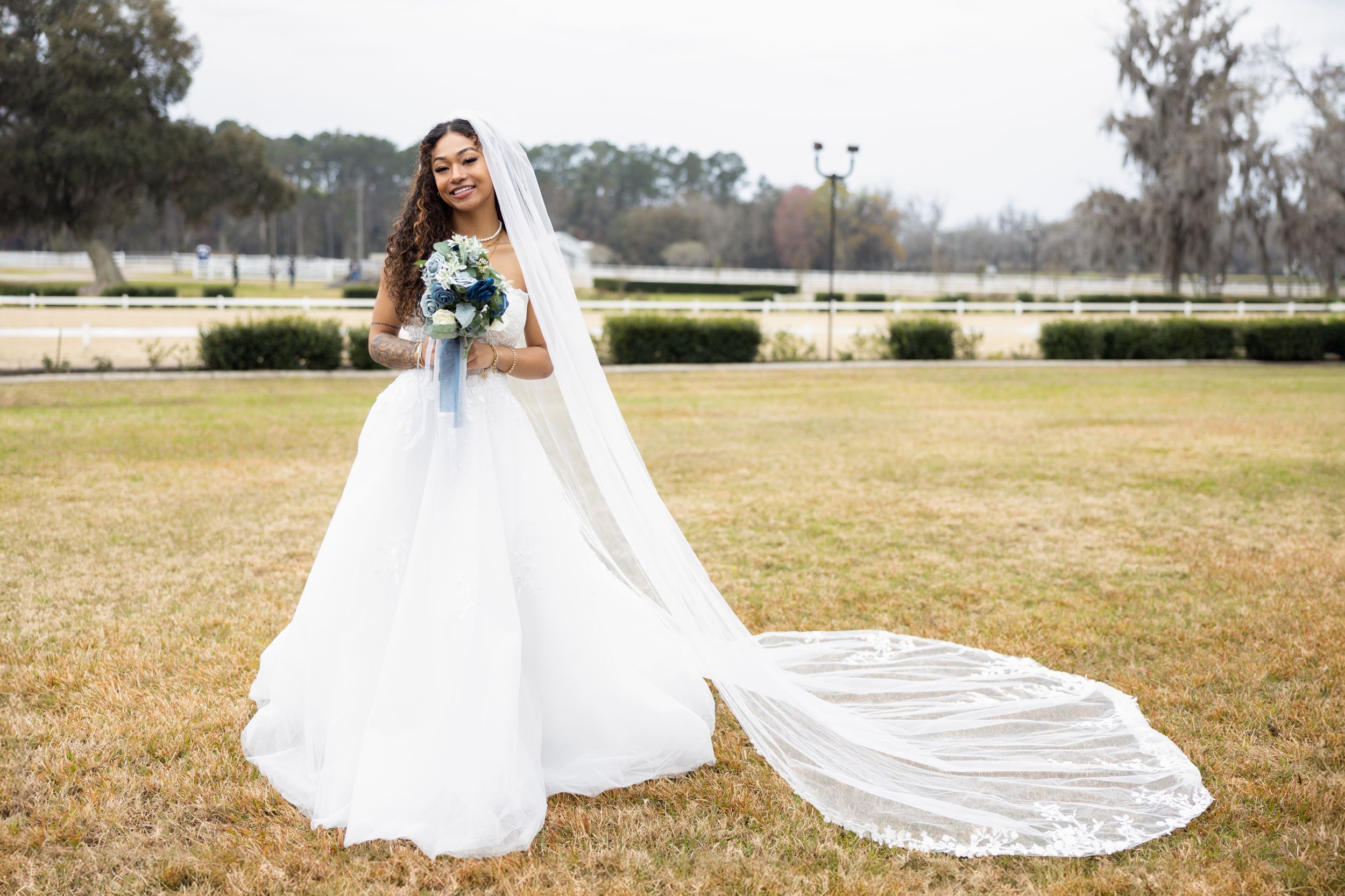 A bride in a flowing white gown with long train poses in a scenic garden setting.